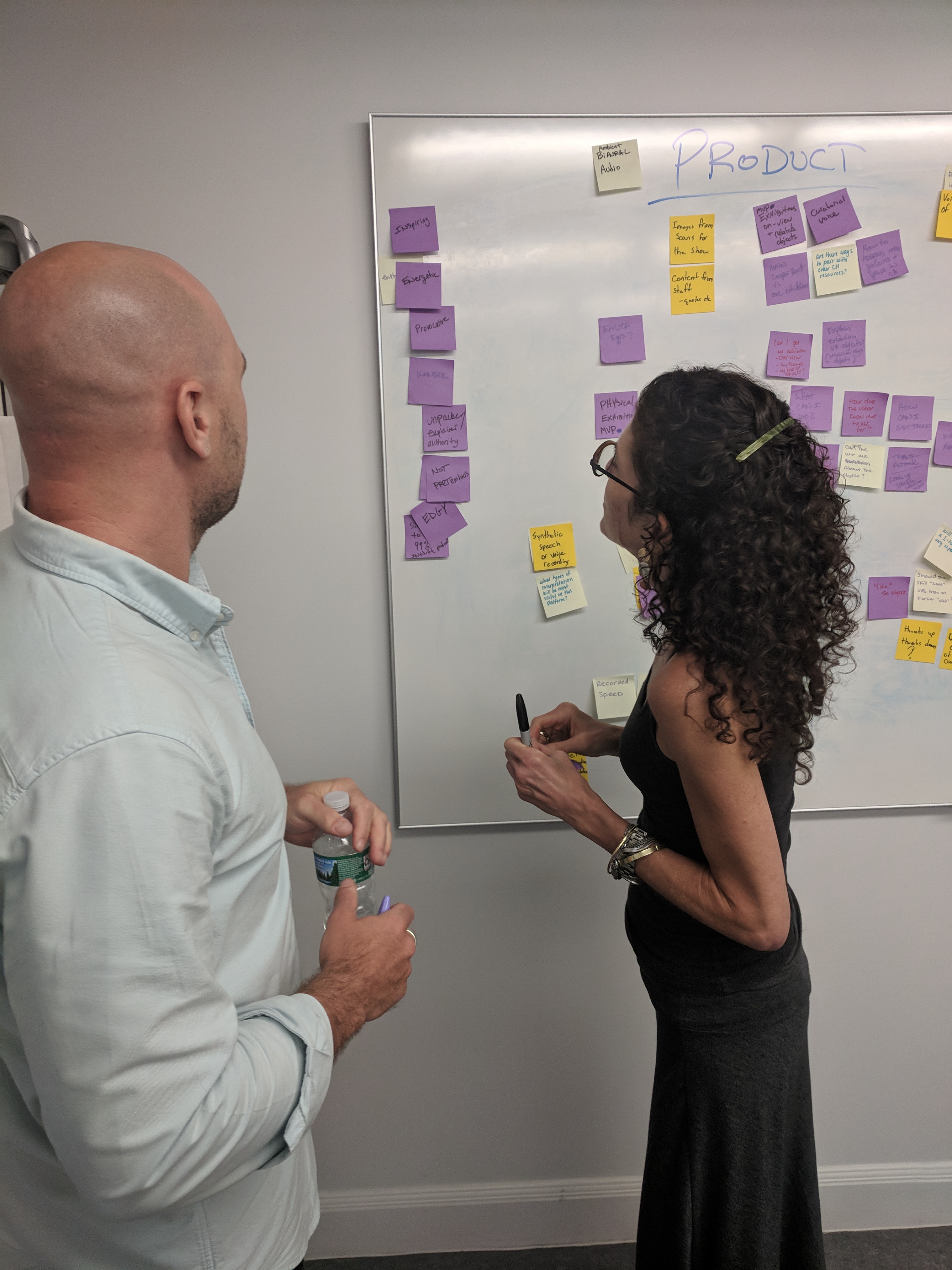 Two people standing at a white board looking at a string of purple post its