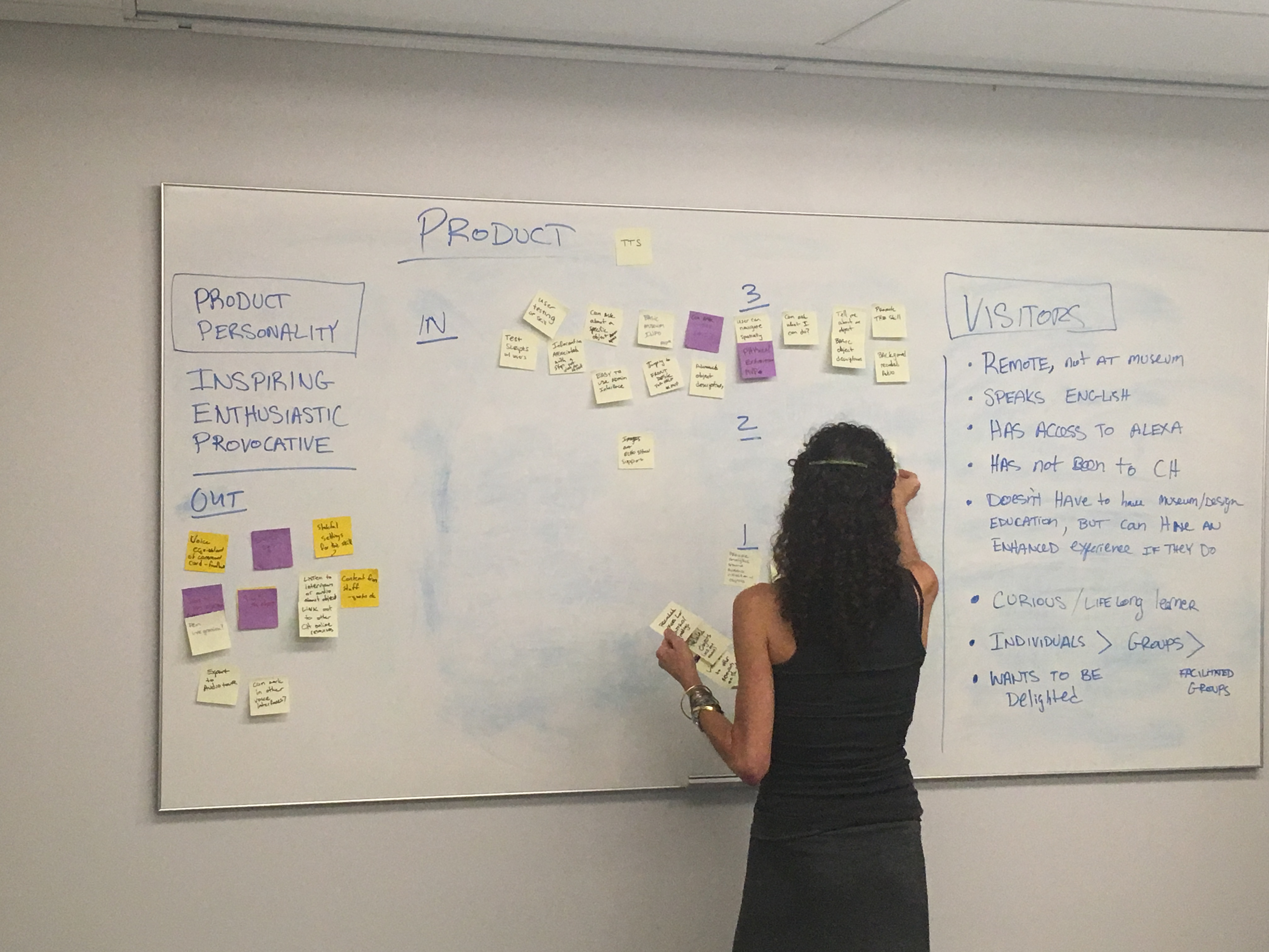 A woman adding post its to a white board with a lot of information on it