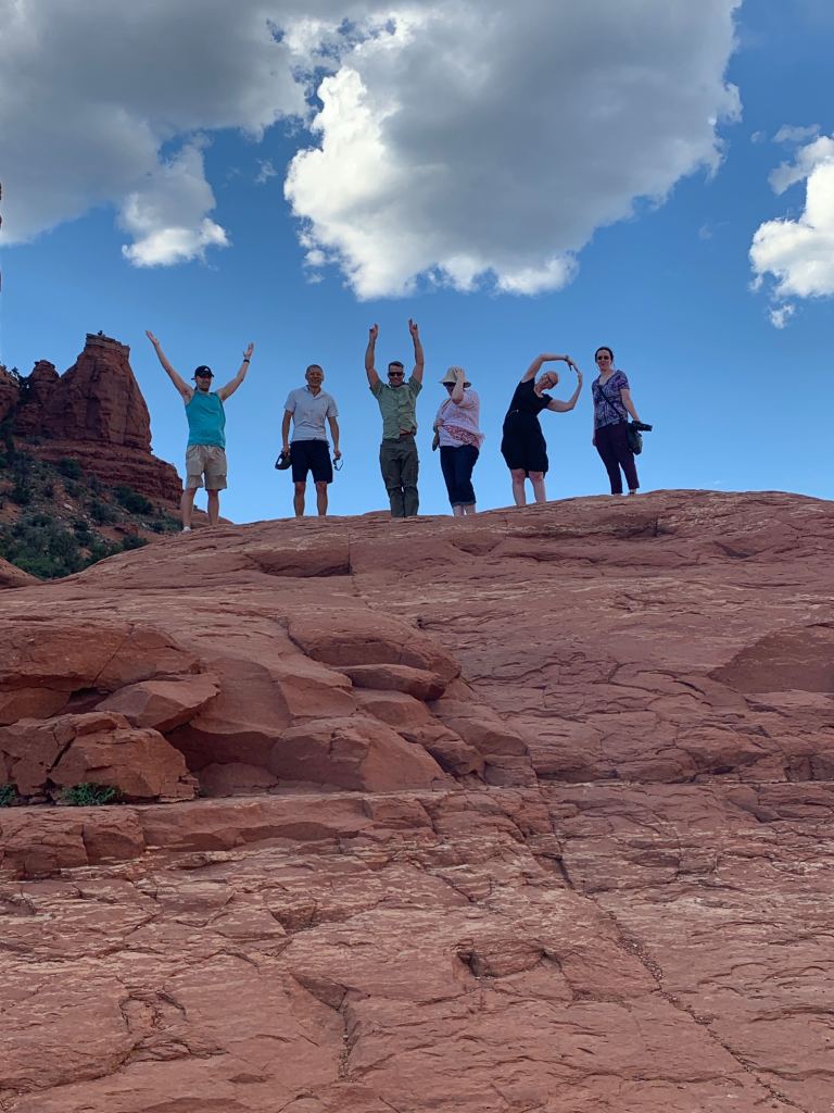 The team stands on top of a large red rock and attempt to spell out "VIP" with their bodies.