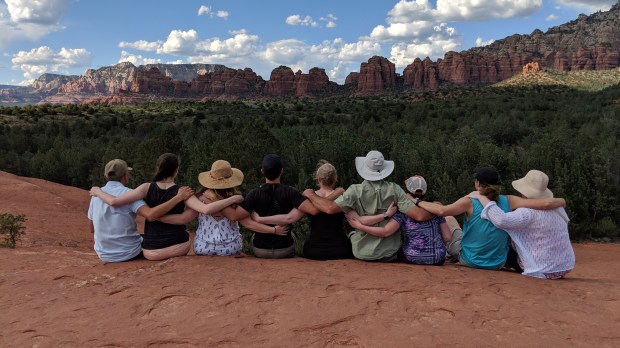 Team VIP sitting down looking out over the red rocks of Sedona. Facing away from the camera with their arms around each other.