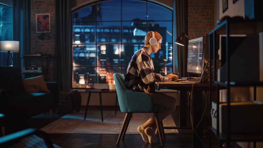 Young woman wearing headphones while working on her desktop at night.