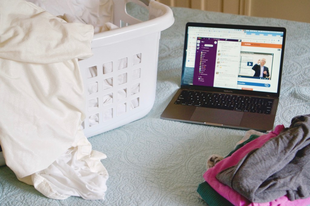 Laptop on bed with laundry basket beside it