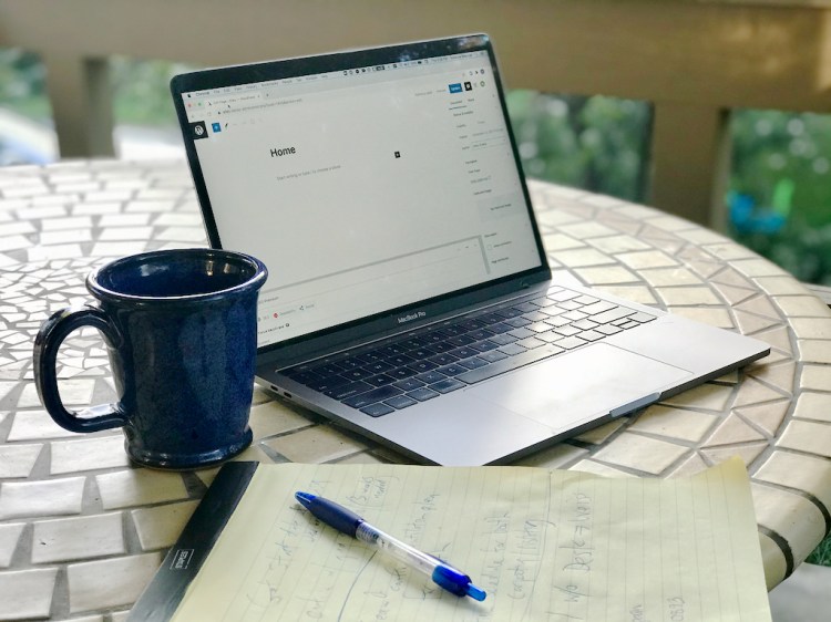 Laptop on table with coffee, pad of paper and pen