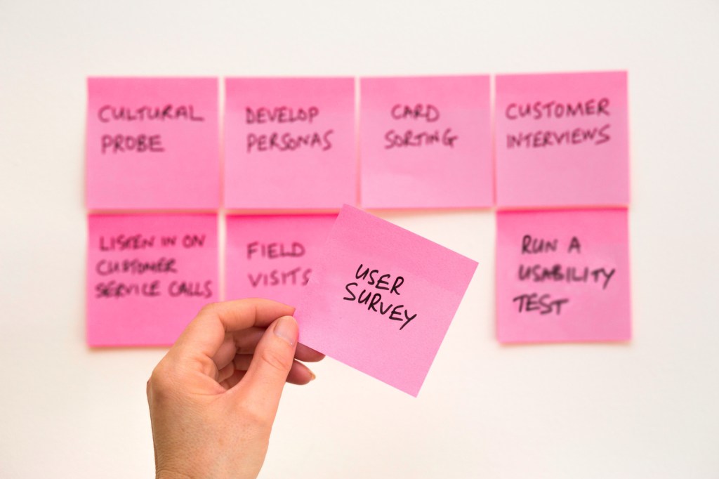 A group of post-its on the wall, with a hand pulling off one that says "User Survey"