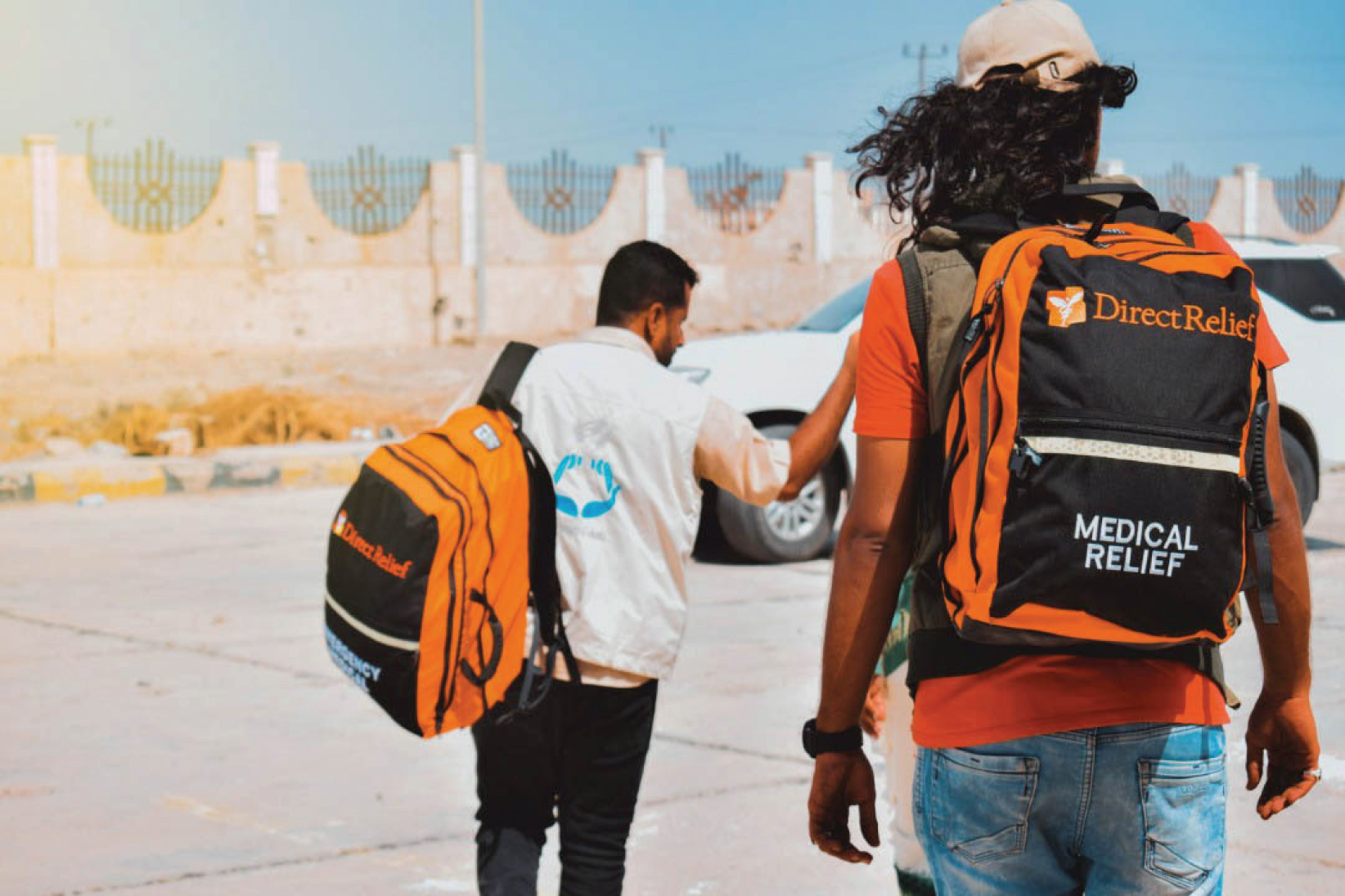 Two men with their back to the camera with orange and black Direct Relief backpacks on