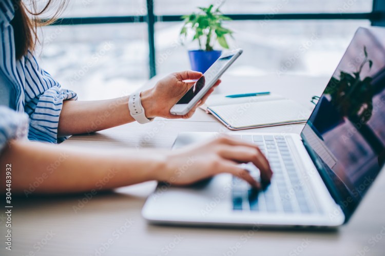 woman looking at her phone and laptop simultaneously